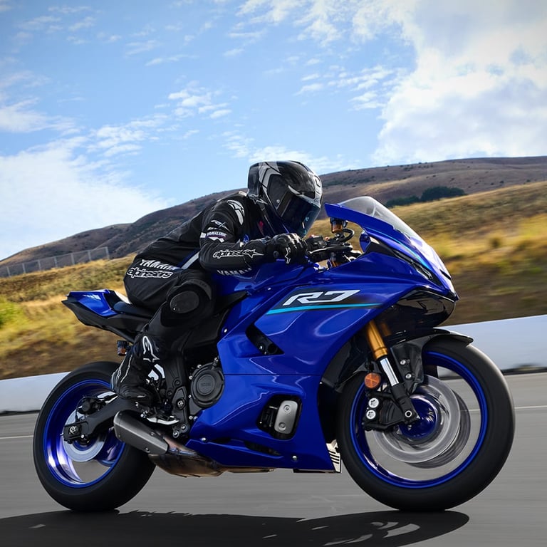 Motorcyclist in black gear riding a blue sport bike on an open road with hills in the background